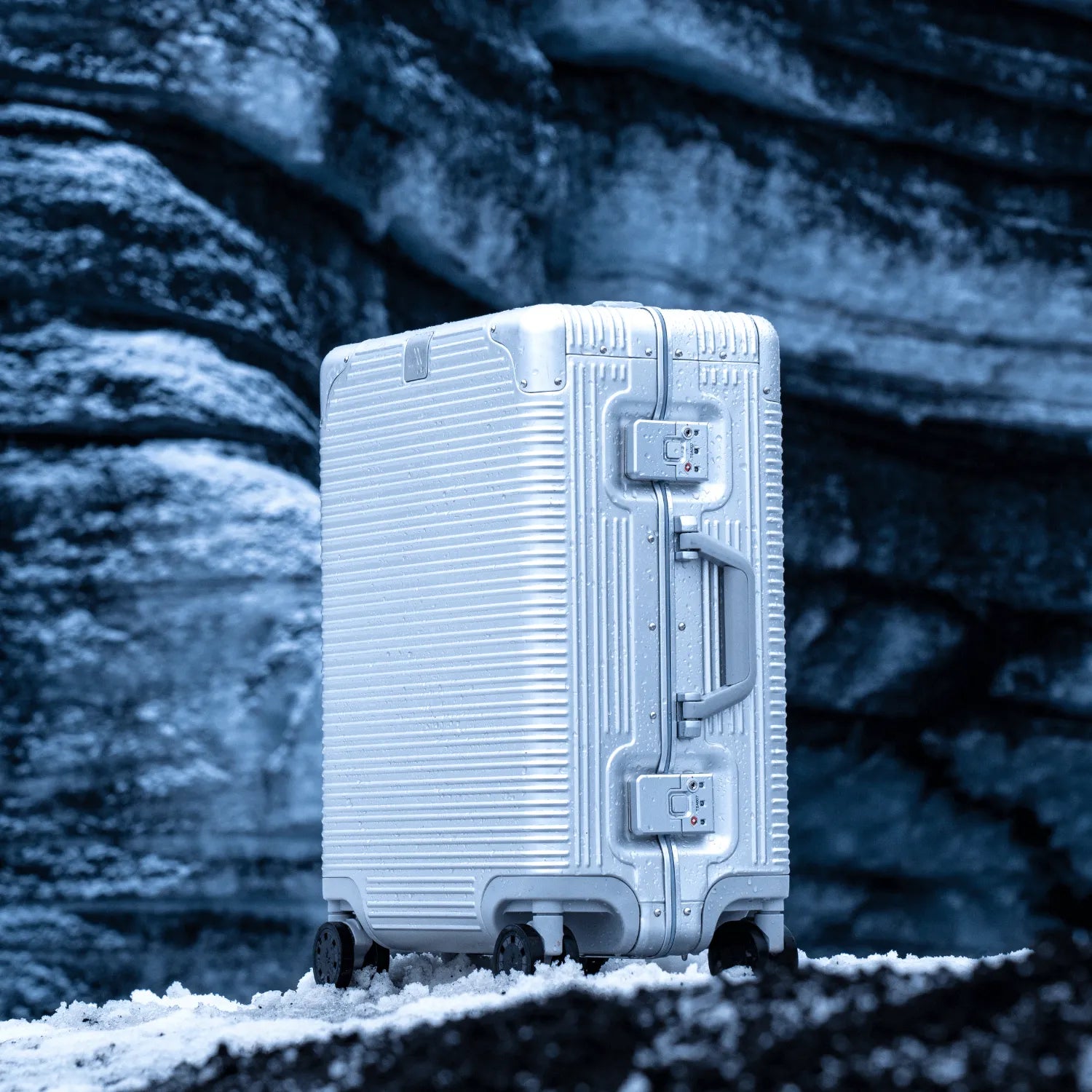 Sleek silver carry-on suitcase against a textured rocky backdrop, perfect for modern travelers.