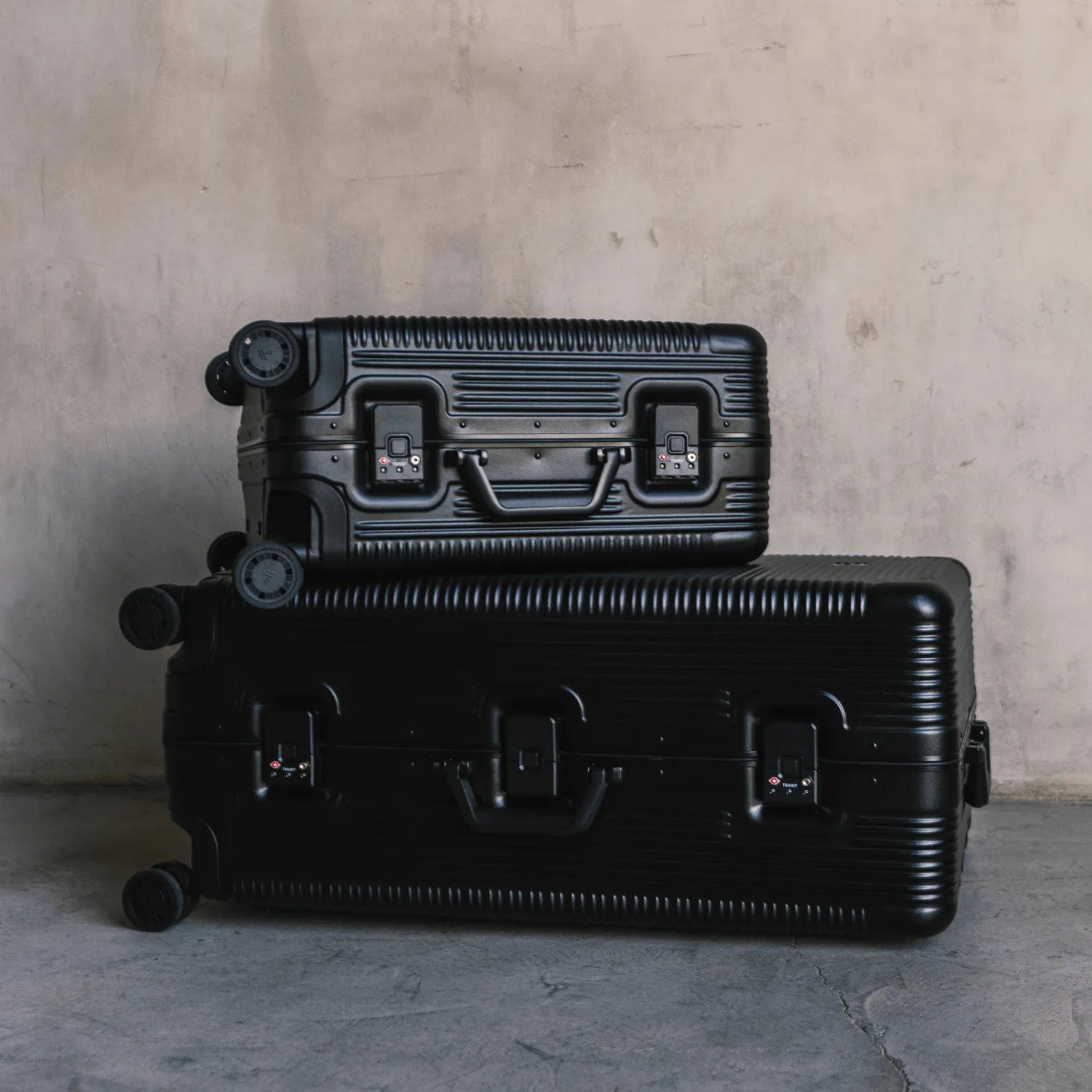 Stylish black luggage stacked against a concrete wall, showcasing modern design and durability for travel enthusiasts.